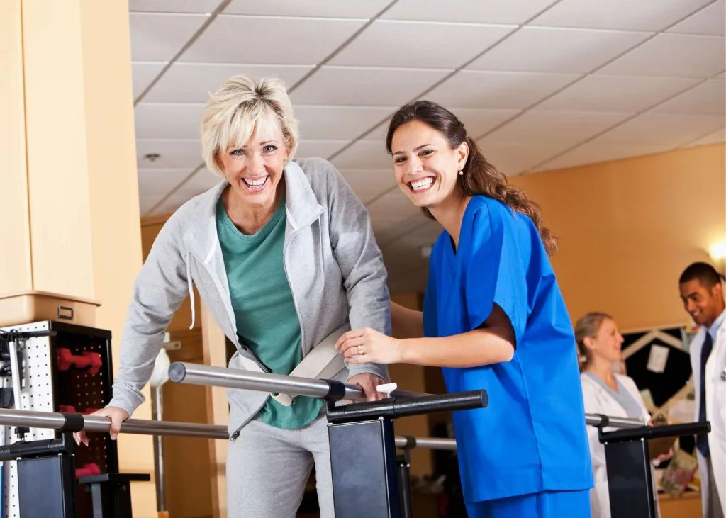 A smiling physical therapist assists an older woman during a rehabilitation session